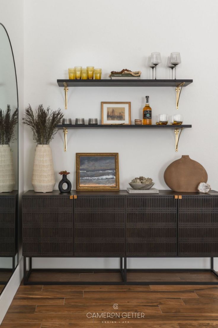 an empty room with shelves and vases on the wall, some pictures are hanging above them