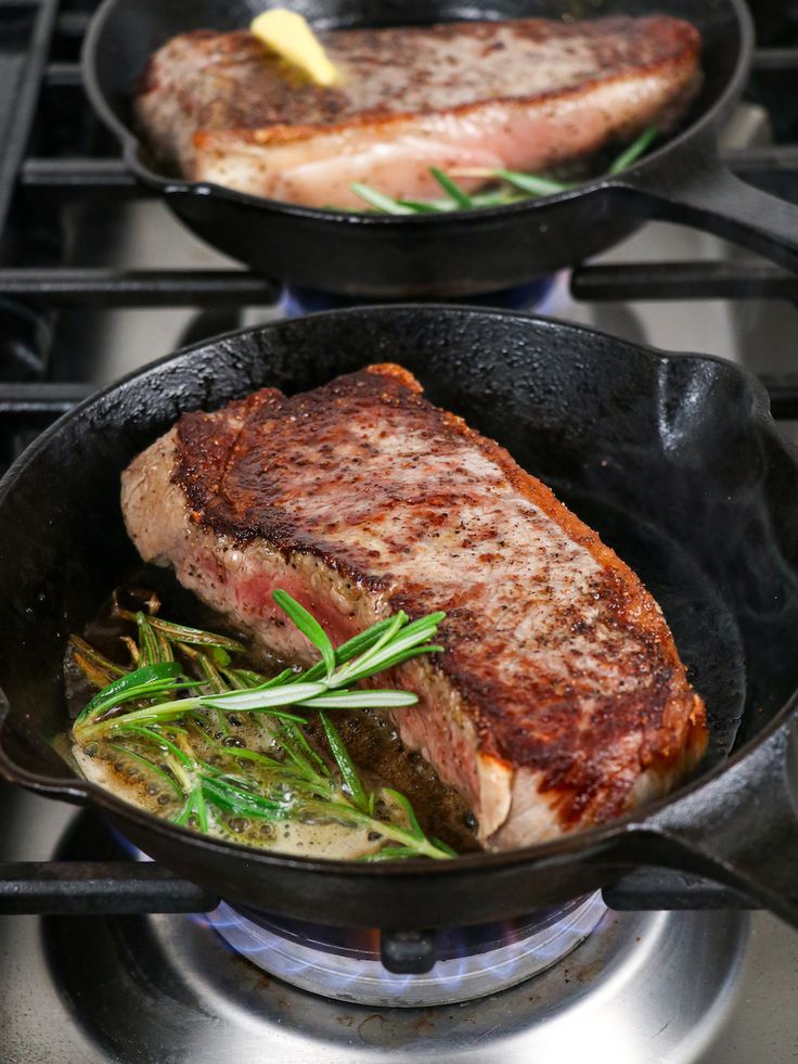 two pans with steak and vegetables cooking on the stove