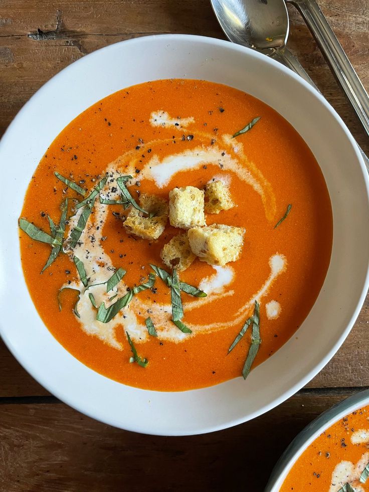 there is a bowl of tomato soup with croutons and herbs in the center