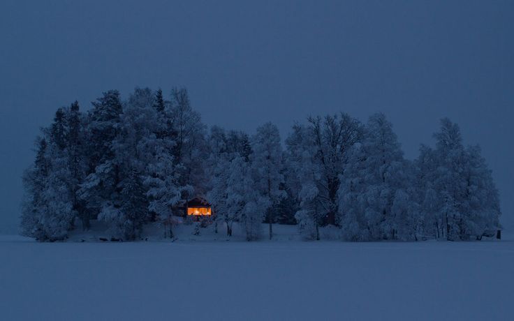 a cabin in the woods is lit up at night with snow on the ground and trees