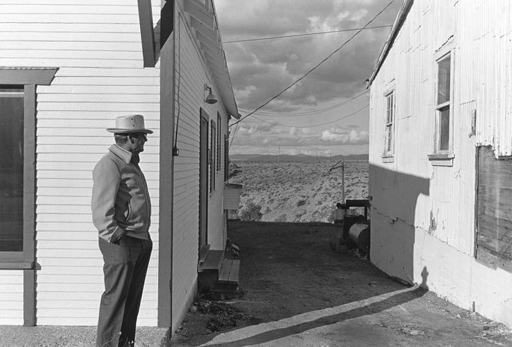 a man standing in front of a house on the side of a road next to a building