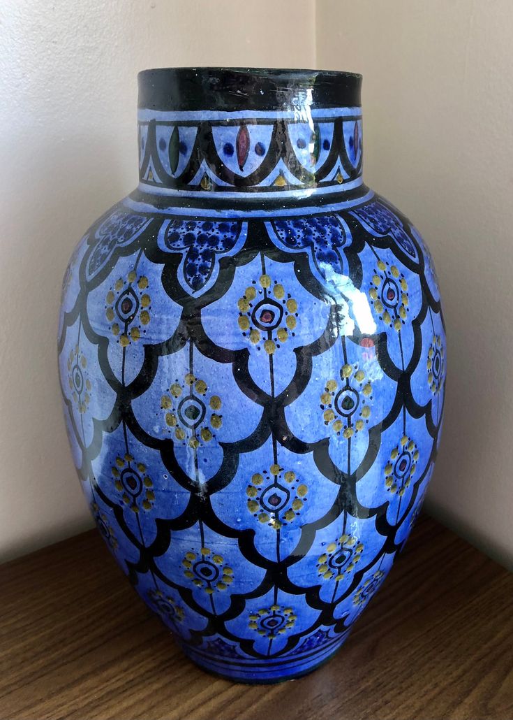 a large blue vase sitting on top of a wooden table next to a white wall