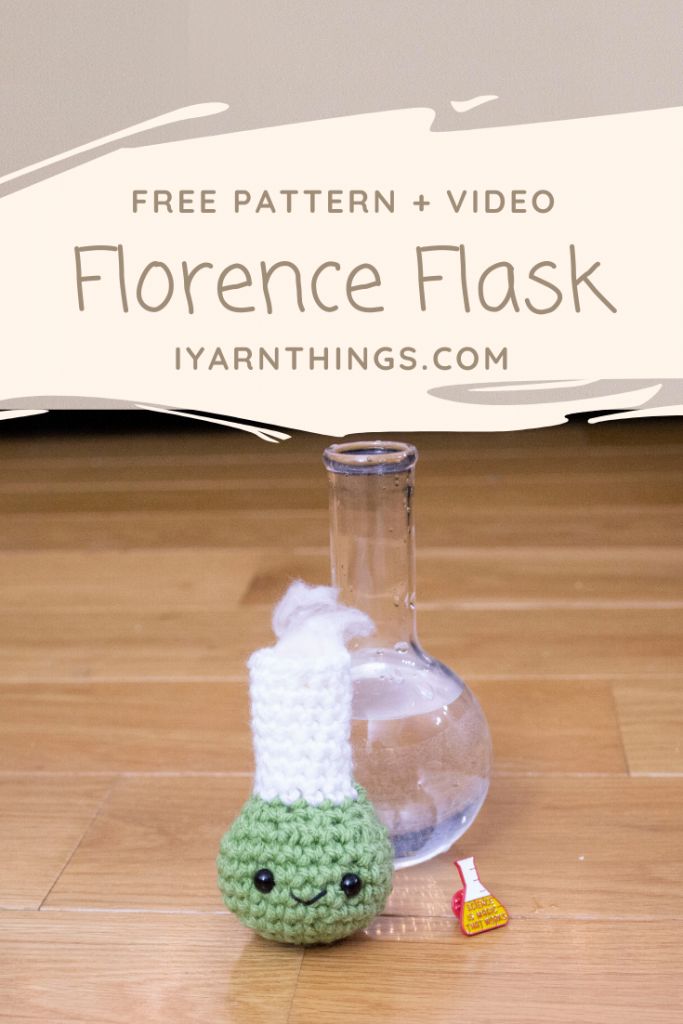 a crocheted green and white object sitting on top of a wooden floor next to a glass bottle