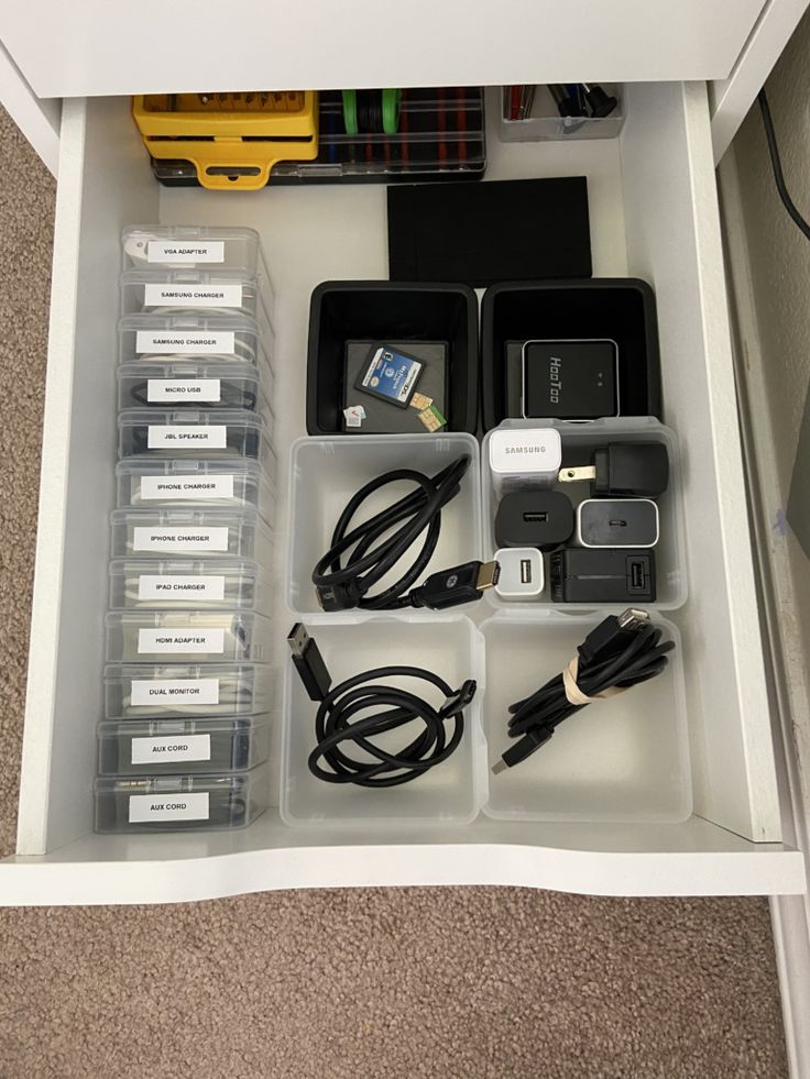 an open drawer with many electronics and cords in it on carpeted floor next to wall