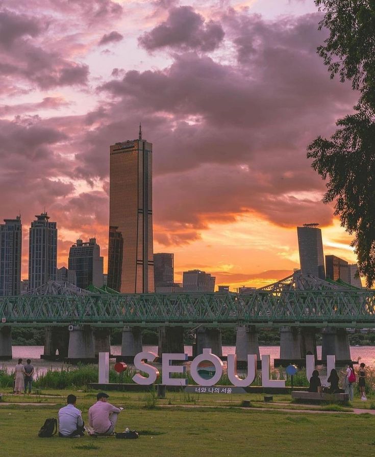 two people sitting on the grass in front of a large sign that says seoulw