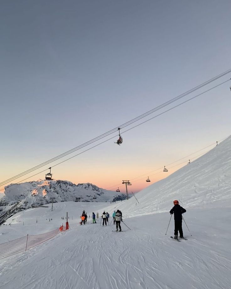 skiers and snowboarders at the bottom of a ski slope as the sun sets