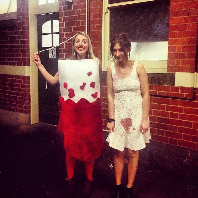 two women standing next to each other in front of a brick building holding up a piece of paper