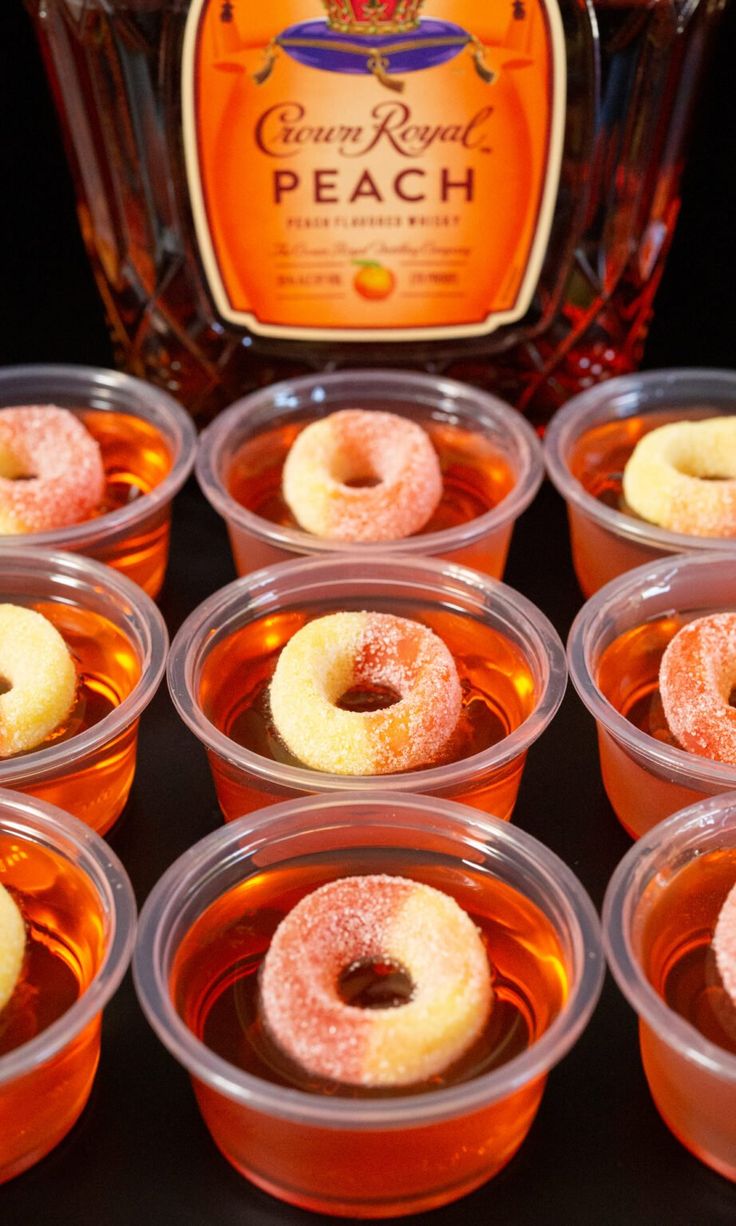 small plastic cups filled with donuts next to a bottle of alcohol on a table