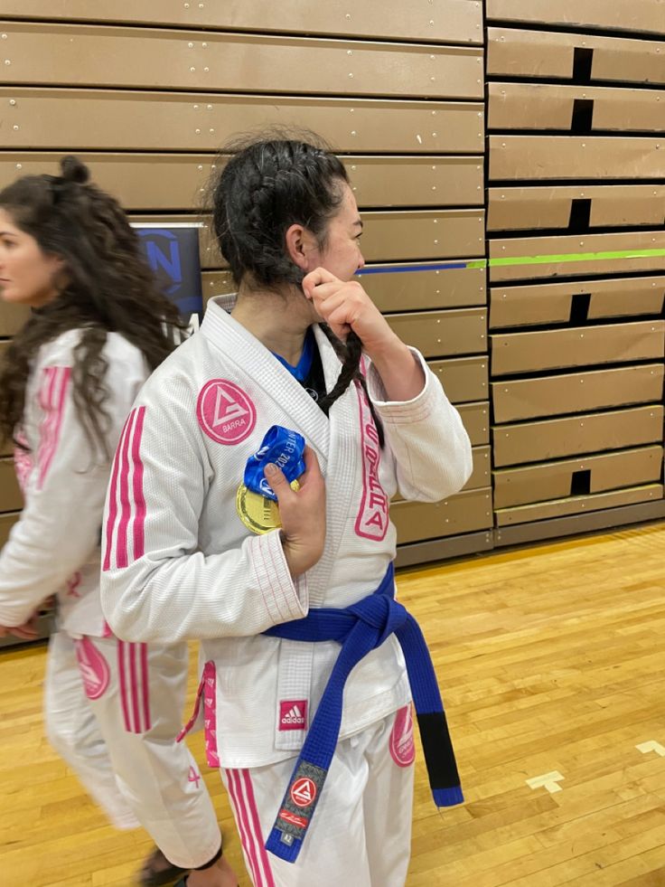 two girls in white and blue uniforms are holding their gold medals as they walk through the gym