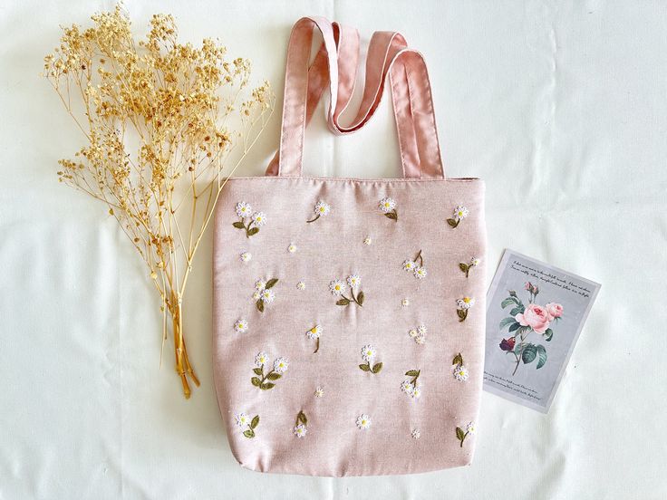 a small pink bag with flowers and a book on it next to some dried plants