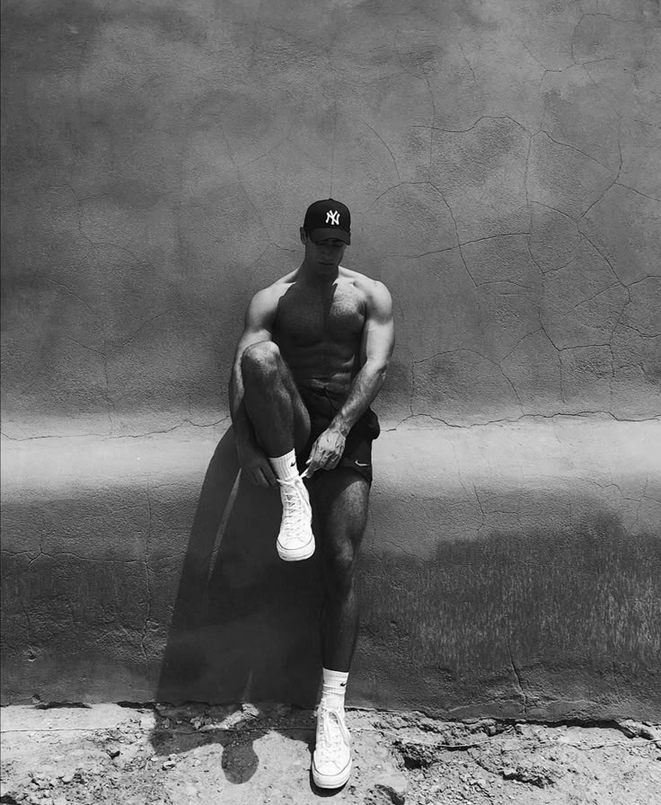 a black and white photo of a man sitting on a wall with his legs crossed