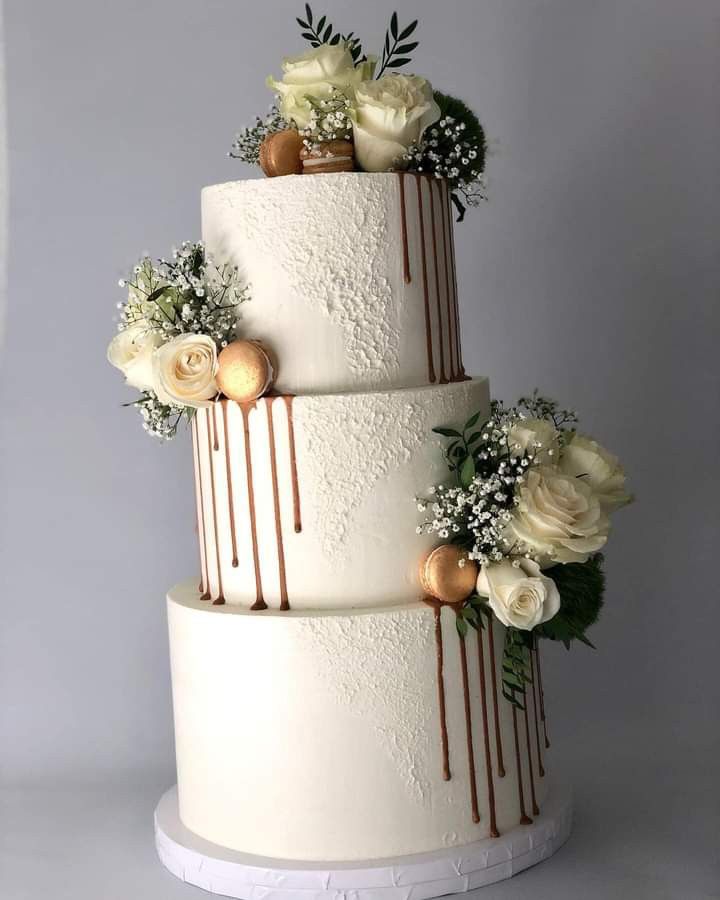 a three tiered wedding cake with white flowers and greenery on the top layer