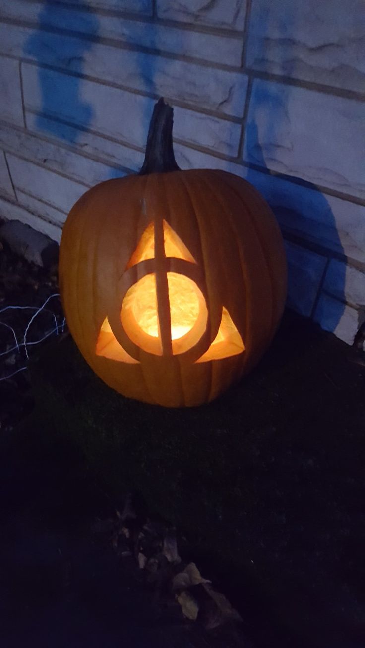 a carved pumpkin sitting on the ground in front of a house with an illuminated letter