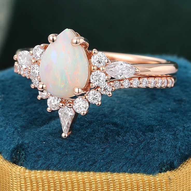 an opal and diamond ring sits on top of a blue velvet cushion