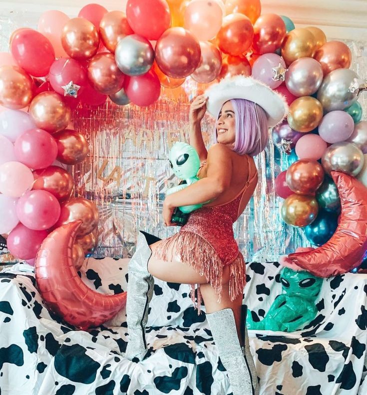 a woman in a cowgirl outfit is sitting on a bed surrounded by balloons