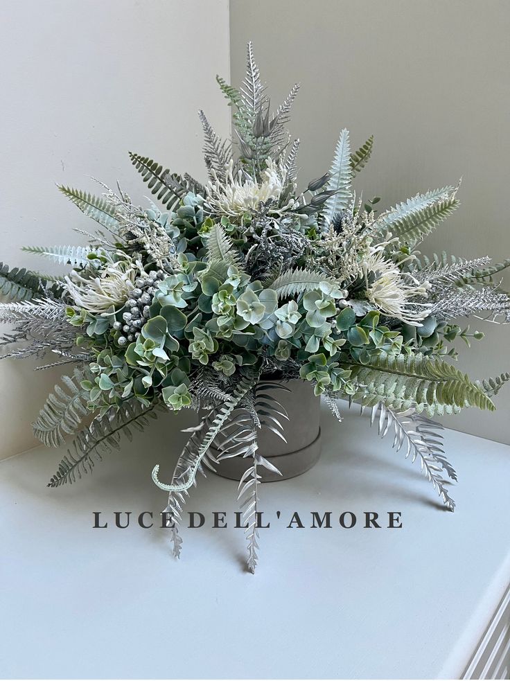 an arrangement of green and white flowers in a metal vase on a table with the words luc dell amore above it