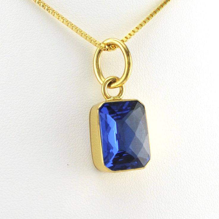 This lab created tanzanite rectangle gemstone is set in alchemía. Gem has a sparkly checkerboard cut. Pendant is 1 3/16 inches long and 1/2 inch wide and is sold separate from the 18k gold fill 1.2mm box chain shown. Alchemía a blend of base metals that looks like 18k gold and will not change color and is hypoallergenic. Style Number: 19209 Metal: Alchemía Gemstone: Lab Created Tanzanite Dimensions: 1 3/16 inches long and 1/2 inch wide Handmade in Mexico Sapphire Jewelry With Rectangular Stone For Gift, Faceted Rectangular Jewelry As A Gift, Rectangular Tanzanite Jewelry For Anniversary, Rectangular Faceted Yellow Gold Jewelry, Gold Faceted Jewelry With Rectangular Stone, Gold Rectangular Faceted Necklace, Gold Faceted Rectangular Necklace, Elegant Rectangular Pendant Gemstone Jewelry, Gold Faceted Rectangular Stone Jewelry