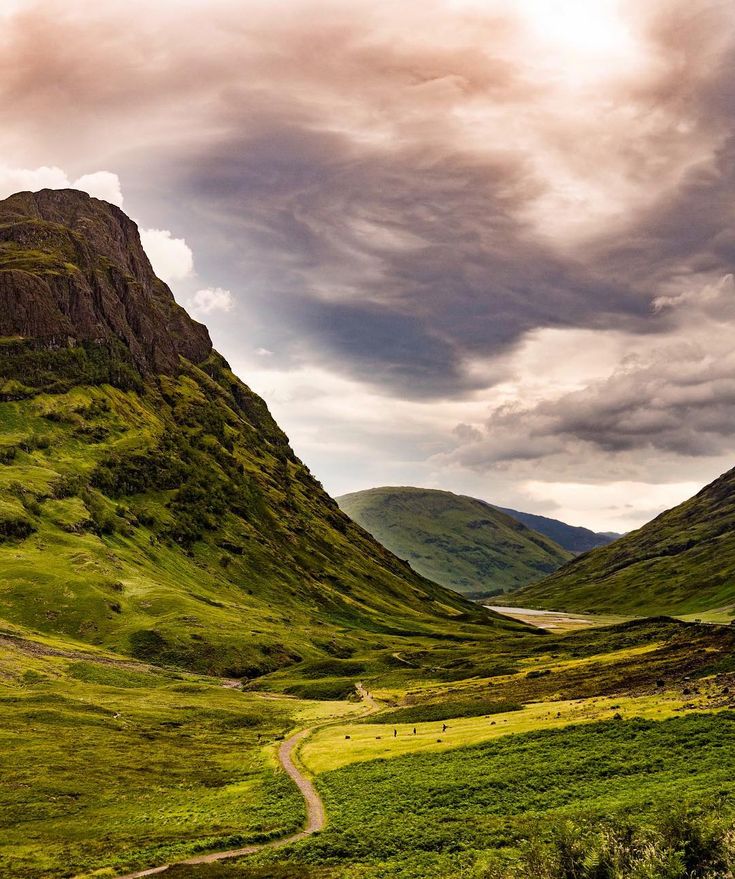 the mountains are covered in green grass and there is a dirt road going through them