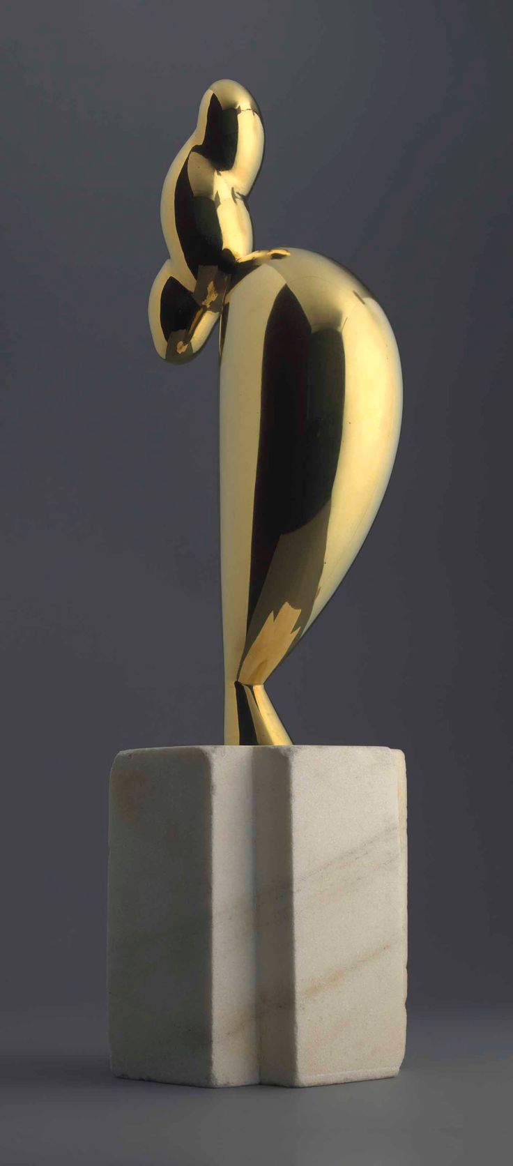 a gold sculpture sitting on top of a white block in front of a gray background