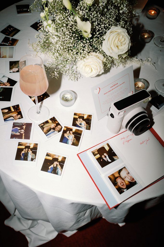 a table topped with pictures and flowers next to a glass of wine on top of a white table cloth