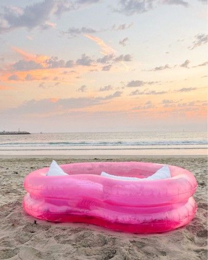 an inflatable float sitting on the beach at sunset or dawn with pink clouds