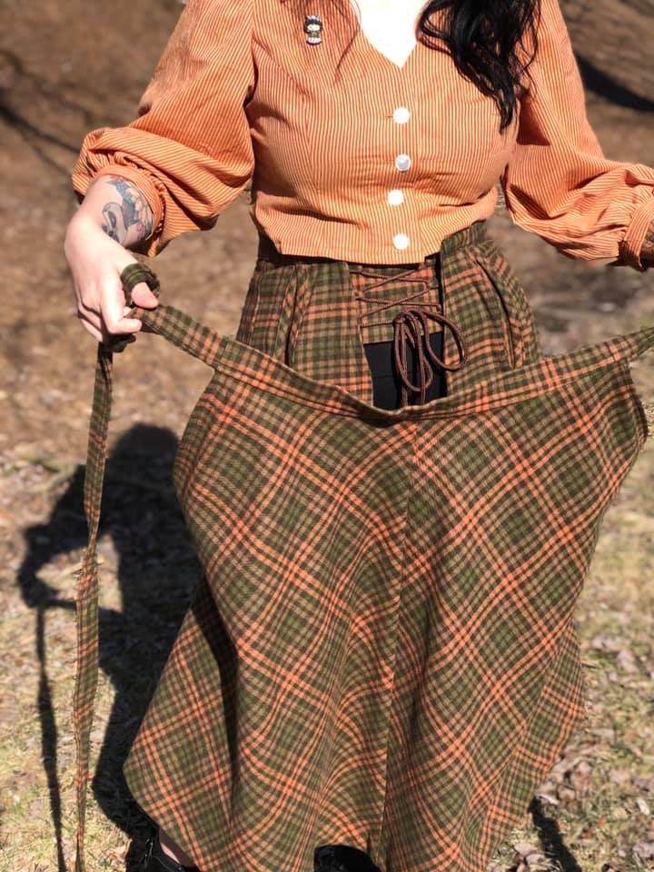 a woman in an orange shirt and green plaid skirt holding a brown dog on a leash