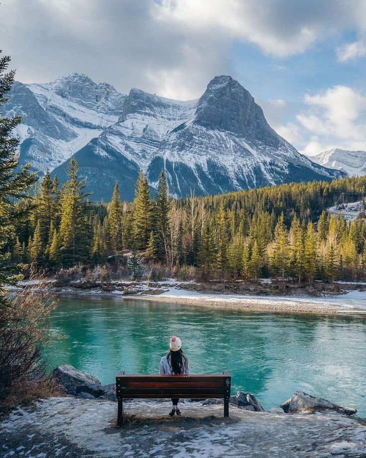 a person sitting on a bench in front of a mountain lake