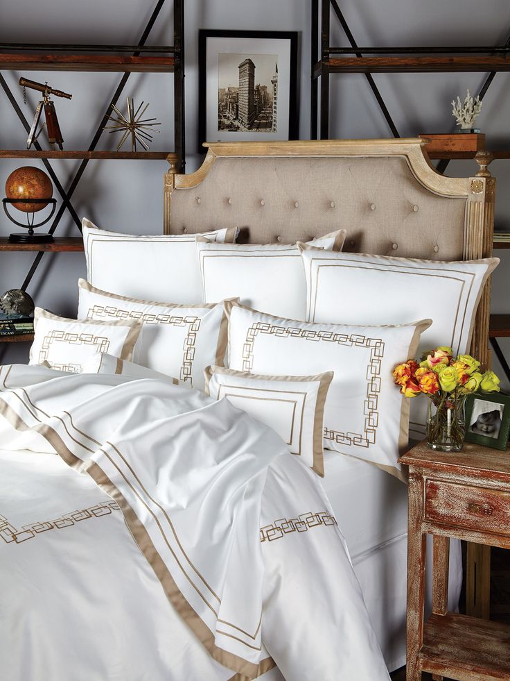 a bed with white sheets and gold trimmings is shown in front of a bookcase