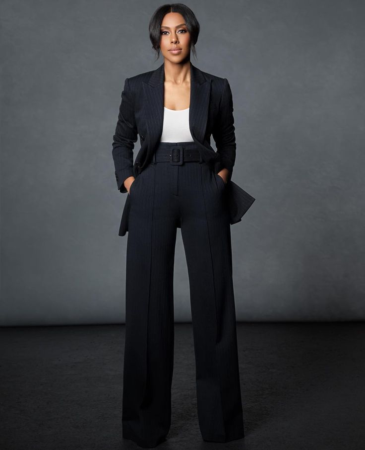 a woman standing in front of a gray background wearing black pants and a blazer