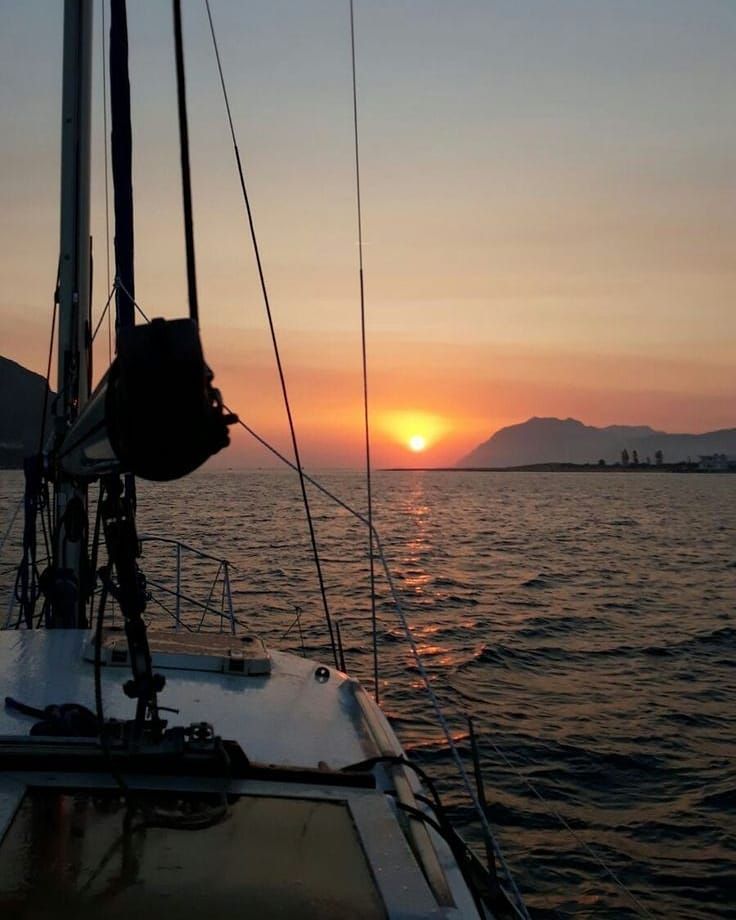 the sun is setting over the ocean with sailboats in the foreground and mountains in the distance