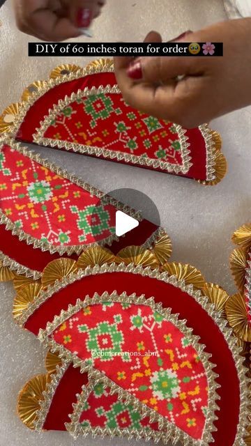 someone is making decorative items with red and gold colors on the table, while another person holds out their hand