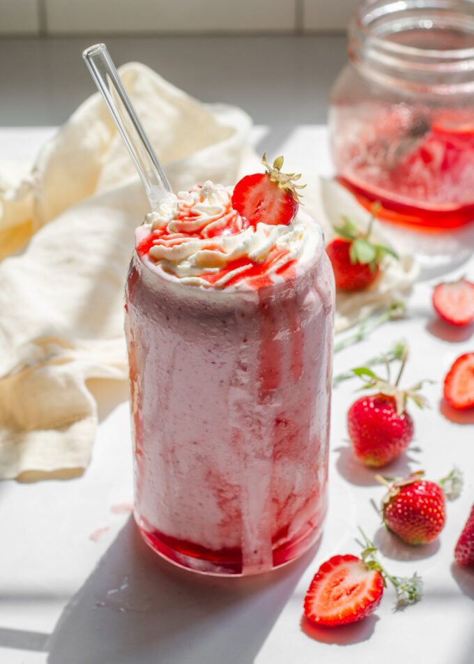 a strawberry milkshake with whipped cream and fresh strawberries on the table next to it