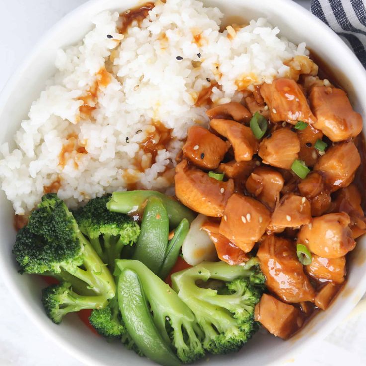 a white bowl filled with rice, broccoli and chicken on top of it