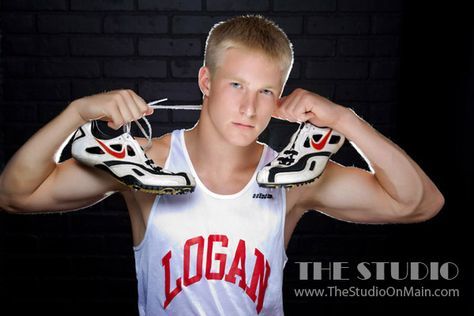 a young man is holding his shoes up to his face and posing for the camera