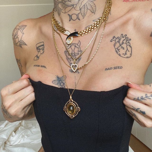 a woman with many tattoos on her chest holding onto a piece of jewelry and looking at the camera