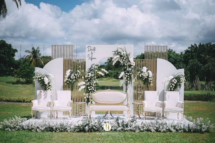 an outdoor wedding ceremony setup with white flowers and greenery on the grass, surrounded by palm trees