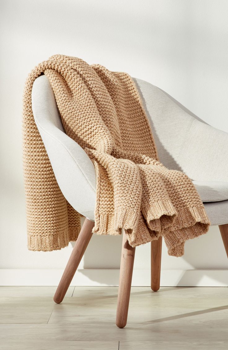 a white chair with a beige blanket on it's back and legs, in front of a white wall