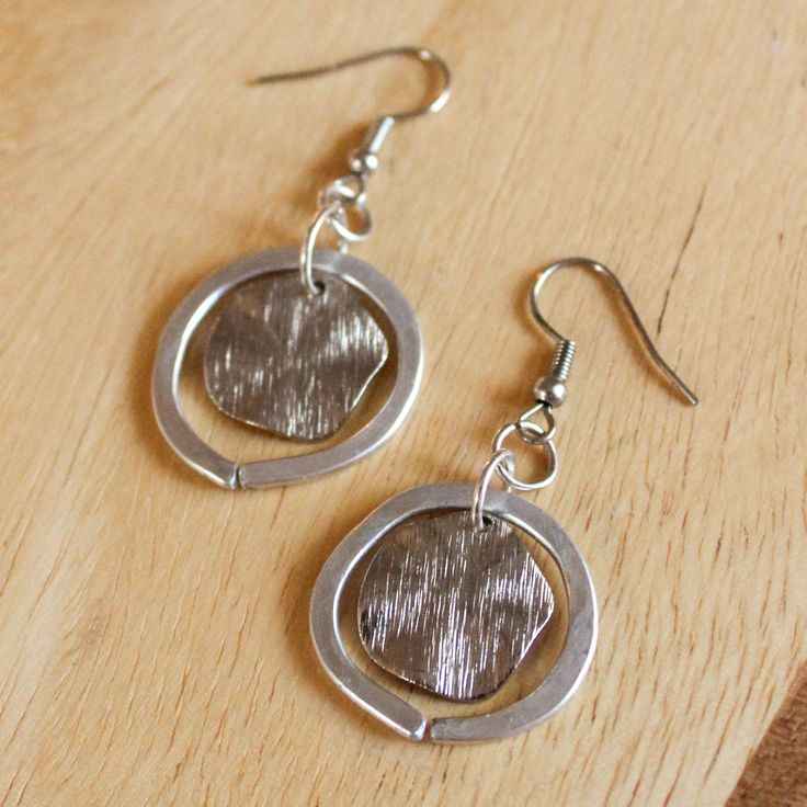 These beautiful silver earrings are handmade with aluminum wire and a dime-sized textured metal center. Perfect for daily wear, special occasions, or as a gift! Please note that these earrings are handmade to order and because of their one-of-a-kind nature may vary from the exact pair shown in the photos. The earrings are sisters, not twins, so both earrings in a set may vary slightly from each other! Nickel-free Circular Metal Jewelry, Nickel-free Pewter Silver Earrings, Silver Pewter Earrings As Gift, Silver Pewter Earrings For Gift, Cadmium-free Silver Hoop Earrings, Silver Metal Earrings For Everyday, Cadmium-free Metal Earrings For Everyday Wear, Adjustable Nickel-free Silver-plated Earrings, Cadmium-free Silver Earrings For Everyday Wear