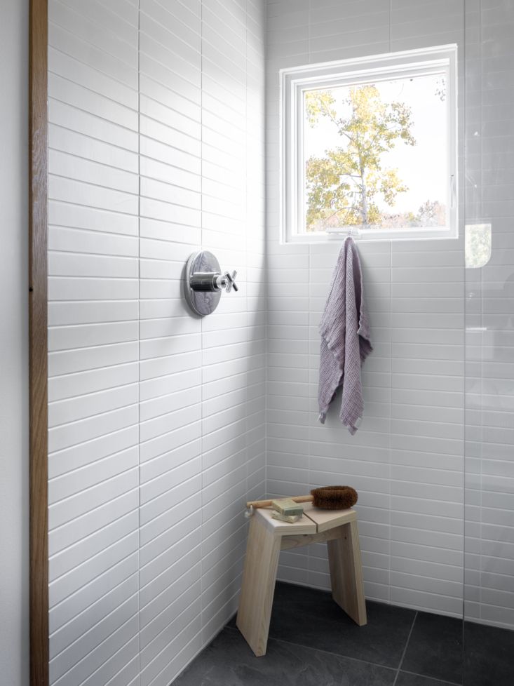 a white tiled bathroom with a bench and window