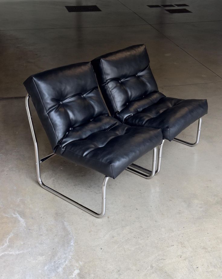 two black leather chairs sitting on top of a cement floor