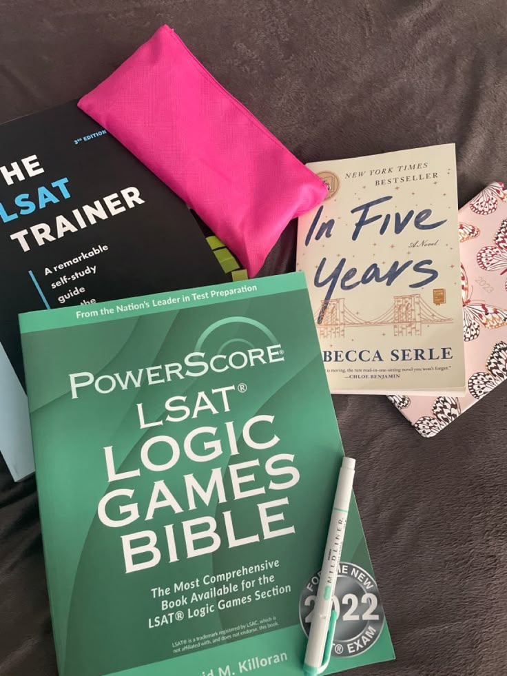 some books are laying on a bed with a pink pillow and a green book bag