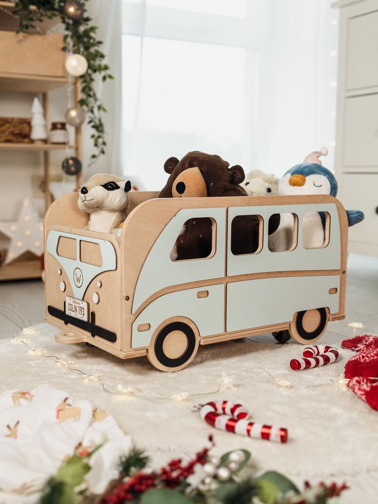 a wooden toy bus with stuffed animals in the front and on the back driving down a christmas decorated floor