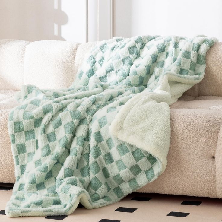 a white couch with a green and white checkered blanket on it's back