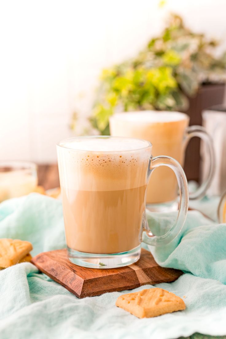 two cups of coffee sitting next to each other on a wooden table with blue cloth