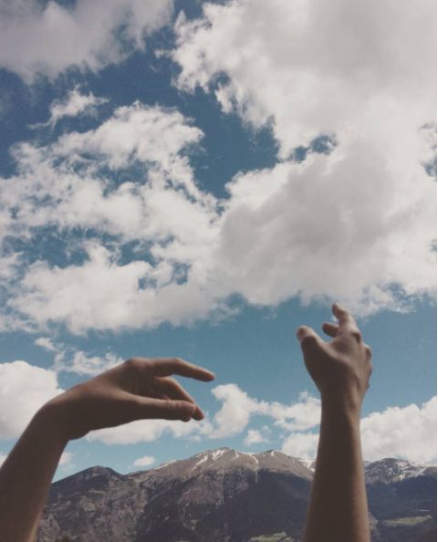 two hands reaching up into the sky to catch a frisbee with mountains in the background