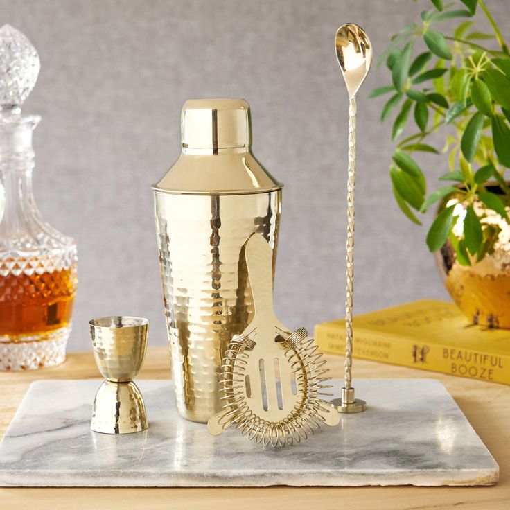 a silver cocktail shaker sitting on top of a table next to two glasses and a spoon