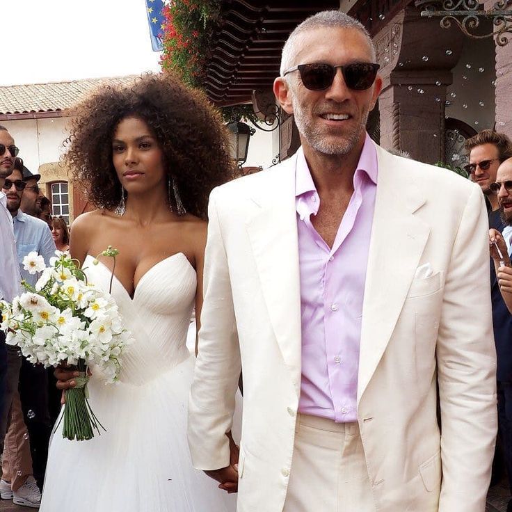 a man in a white suit and woman in a white dress walking down the street