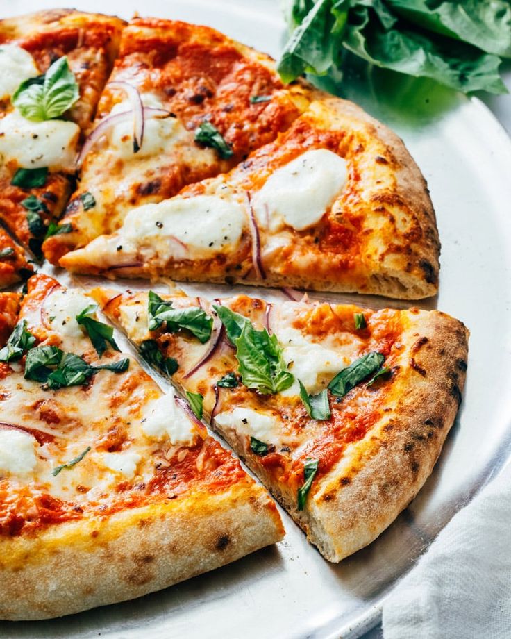 homemade goat cheese pizza on a white plate with lettuce and spinach leaves