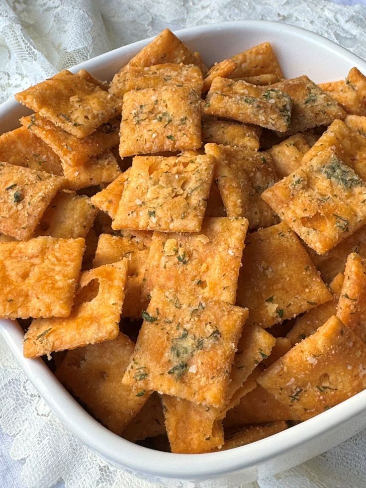 a white bowl filled with cheesy crackers on top of a table cloth