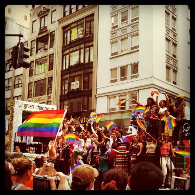 a large group of people standing in front of a tall building holding rainbow colored flags